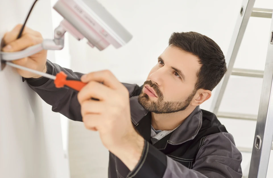 Homme installant un système d'alarme de sécurité à la maison sur un mur blanc à l'intérieur, gros plan