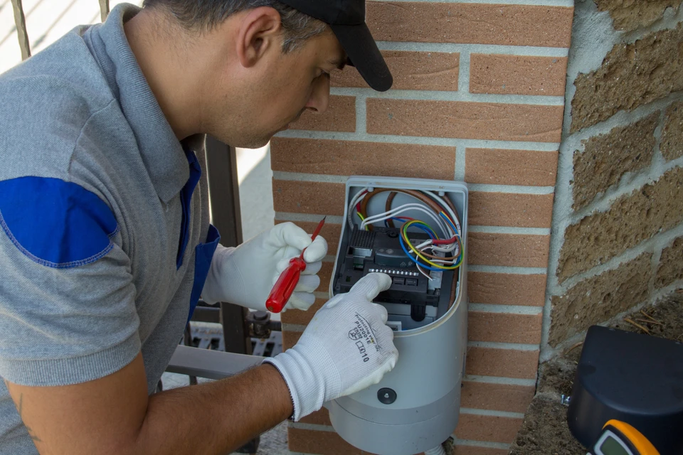 Un technicien en tenue professionnelle inspectant et installant un système de motorisation de portail, tenant un mètre ou outil de mesure, effectuant une visite de diagnostic sur site devant un portail résidentiel ou professionnel en Loire-Atlantique. L'image doit montrer l'aspect professionnel et technique de l'installation, avec la porte ou portail comme élément central de la scène.