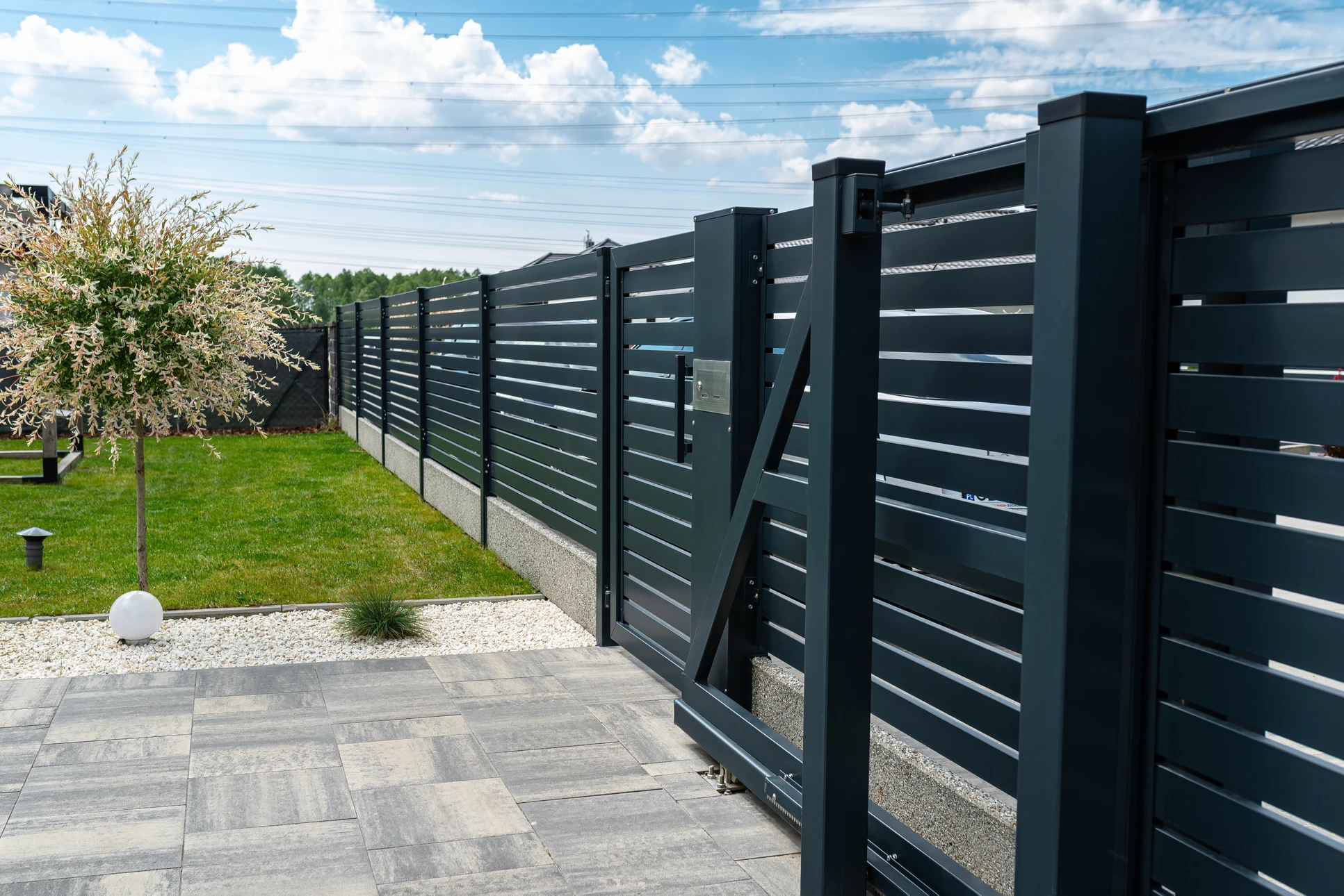 Portail résidentiel en fer forgé noir à double vantaux avec motifs décoratifs, installé entre piliers en pierre naturelle
